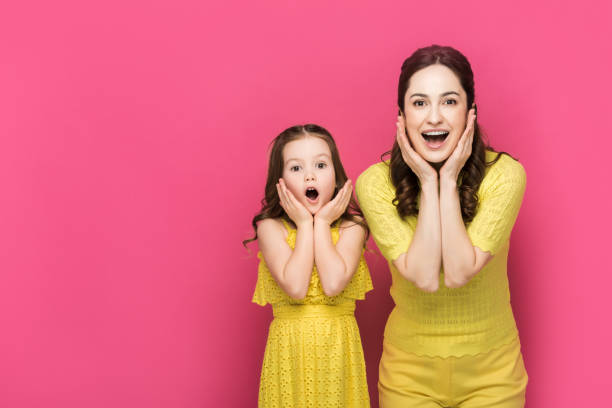 istock excited mother and daughter looking at camera isolated on pink 1214319400