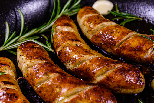 Roasted sausages with rosemary twigs and garlic in cast iron grill pan