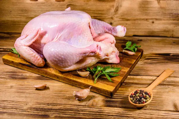 Wooden cutting board with whole uncooked chicken, garlic and spices