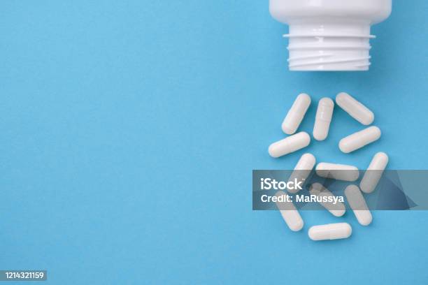White Capsules Falling From The White Bottle On Blue Paper Background Concept Of Pharmacy Stock Photo - Download Image Now