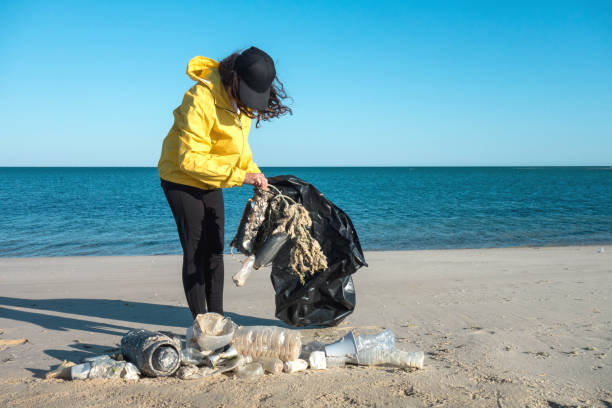 istock Woman picking up trash and plastics cleaning the beach with a garbage bag. 1214323076