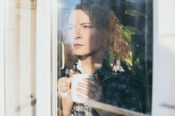 Young blonde woman looking out of the window with a concerned expression on her face stock photo