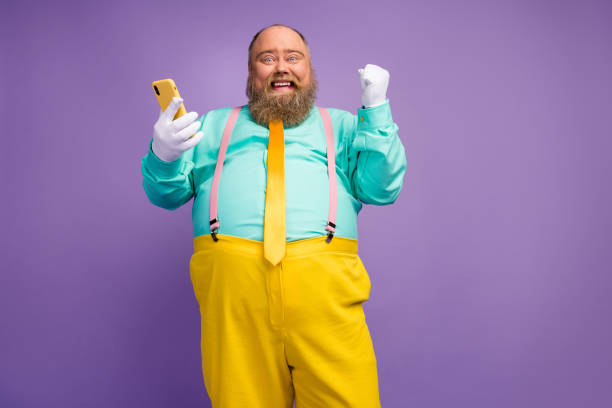 istock Low angle view photo ecstatic bearded man big belly use smartphone achieve win loterry raise fists scream wear white gloves teal pink suspenders gloves isolated bright purple color background 1214326363