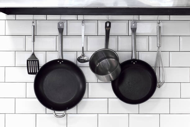 kitchenware, pans, bowls, with cutlery hanging on a white brick wall in a row