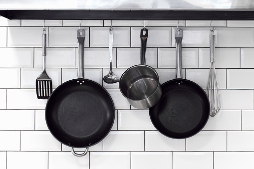kitchenware, pans, bowls, with cutlery hanging on hooks on a white brick wall in a row