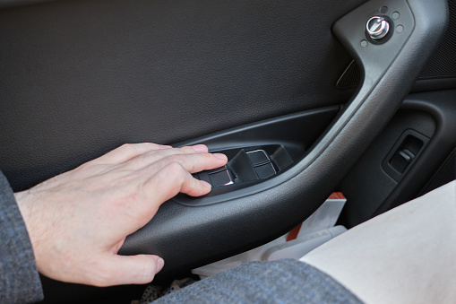 A man in a modern car. The hand presses a button to adjust the windows of the door. Close up.