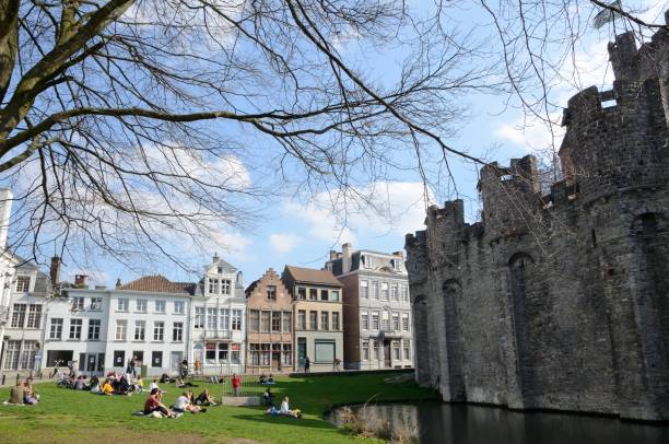 Ghent, Belgium - March 31, 2019: People  at the grass beside the banks of lake beside the medieval castle in Ghent,  the capital  of the East Flanders province in Belgium.