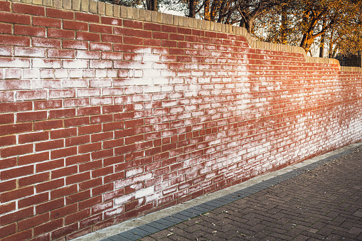 A long red brick wall stained with white efflorescence, a crystalline of salt, formed due to water being present in or on the bricks.