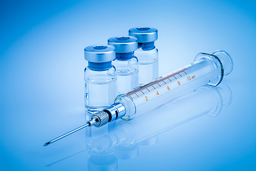 two ampoules of vaccine with a syringe on a blue background.