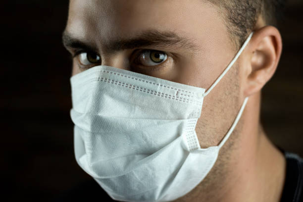 istock young man in a mask from a virus on a dark background 1214335379