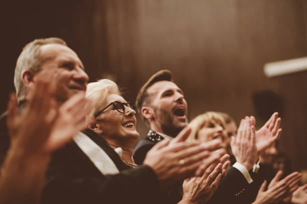 Standing ovation in the theater Smiling audience clapping in the opera. Focus on man shouting. Men and women are watching theatrical performance. They are in elegant wear. classical concert photos stock pictures, royalty-free photos & images