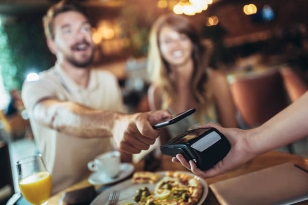 istock Happy couple using mobile phone and making contactless payment in a restaurant 1214336941