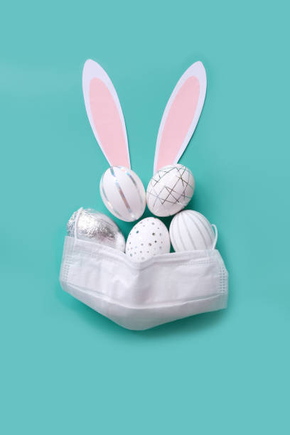 istock Easter time in quarantine concept. Face mask on easter eggs on the table on a white background. 1214340649
