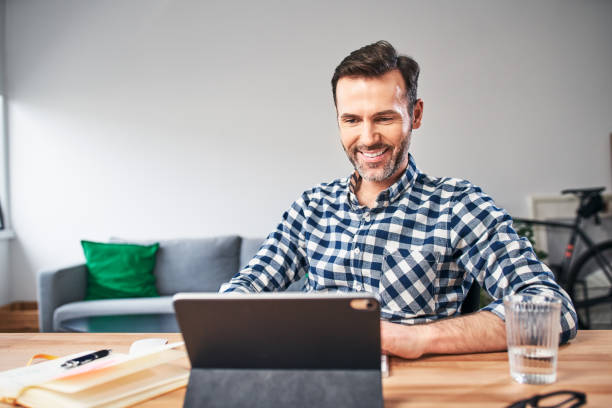istock Portrait of smiling man working from home looking at digital tablet 1214342086