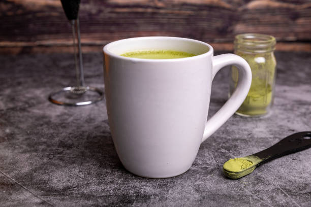 Cup or fresh, organic Matcha Latte with matcha powder next to it.