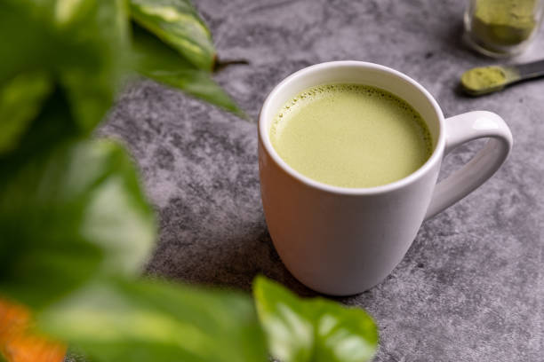 Cup or fresh, organic Matcha Latte with matcha powder next to it.