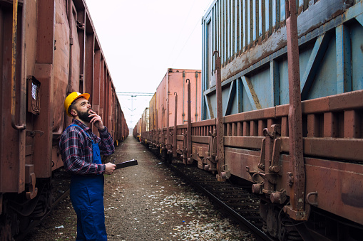 Worker inspecting cargo shipping containers. Railway man checking train trailers before departure.