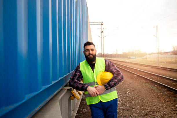 Portrait of railway worker standing by the freight train transporting cargo shipping containers at station.
