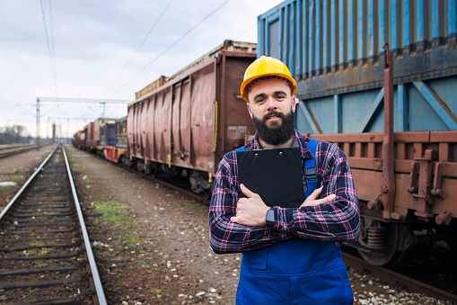 Portrait of railway man worker with departure schedule. In background railway tracks and freight train.