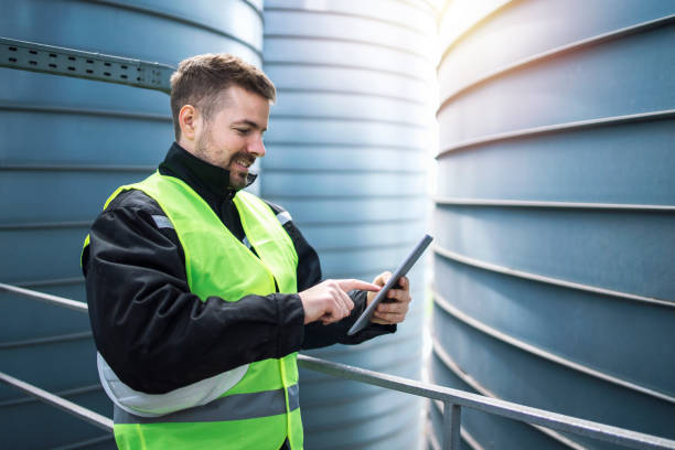 fabrikarbeiter mit tablet-computer in industriellen fabrikgebäude. im hintergrund silo-lagerbehälter. - silo tank stock-fotos und bilder