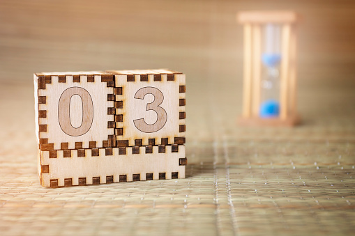 Calendar, wooden cube with date 3 and an empty space for the month, on an abstract woven hourglass background.