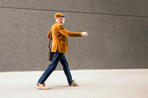 Fashionable Senior Man Outdoors wearing laptop bag walking
