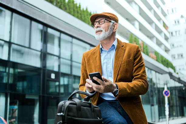 istock Senior Man Outdoors with glasses sitting in front of office using phone 1214350988