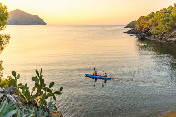 High angle distant view of friends paddling three kayaks in Mediterranean Sea along the Costa Brava at dawn.