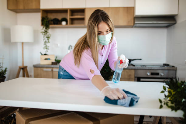 istock Young woman sanitizing her dining table while wearing mask for protection of strong disinfectant 1214354599