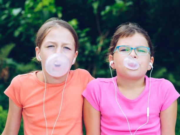 dziewczyny dzielące się słuchawkami do słuchania muzyki. siostry żuć gumę i zrobić balony z niego - chewing gum audio zdjęcia i obrazy z banku zdjęć