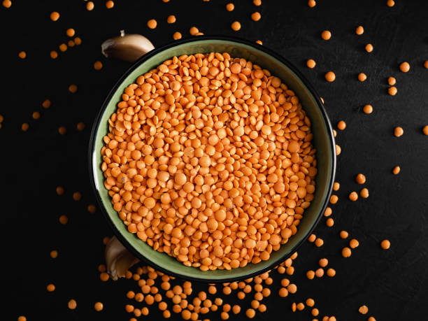Bowl with seeds of red lentils on a black stone background. Lentil seeds and cloves of garlic are scattered next to the bowl. Flat lay stock photo