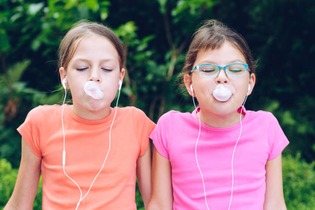 dziewczyny dzielące się słuchawkami do słuchania muzyki. siostry żuć gumę i zrobić balony z niego - chewing gum audio zdjęcia i obrazy z banku zdjęć