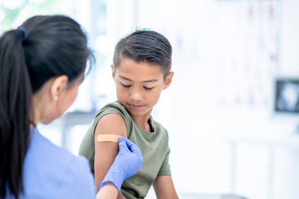 Young Boy Visits Doctor A young mixed-race boy visits a female doctor.  The Doctor is placing a bandage on the boy's arm where he received a vaccine injection. flu vaccine photos stock pictures, royalty-free photos & images