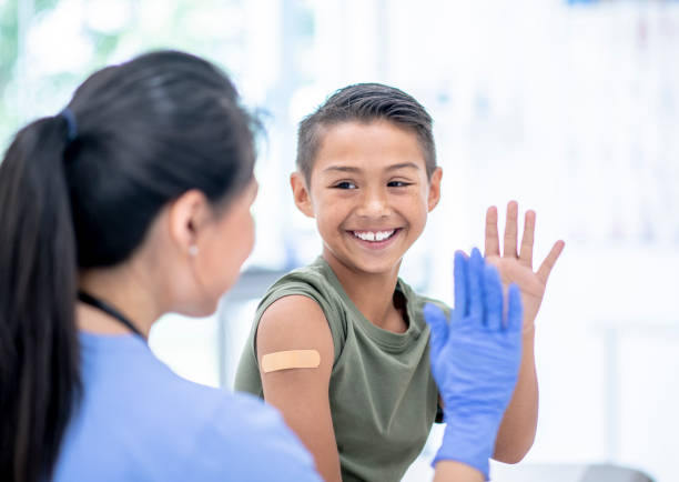 Young Boy Visits Doctor stock photo A young mixed-race boy visits a female doctor.  The boy has a bandage on his arm where he received a vaccine injection.  He is about to high-five the female doctor. flu vaccine photos stock pictures, royalty-free photos & images