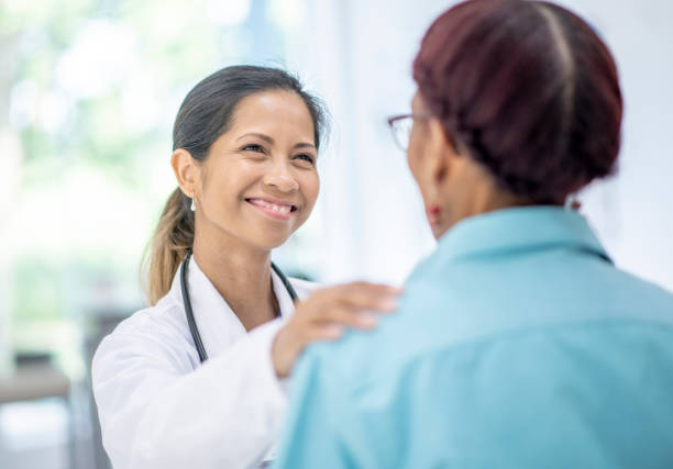 Elderly Woman Visits Doctor stock photo An elderly African American woman sits with her back to the camera, across from a mixed-raced female doctor during a visit.  The Female doctor is wearing a white lab coat and has a stethoscope around her neck. cambodian ethnicity stock pictures, royalty-free photos & images