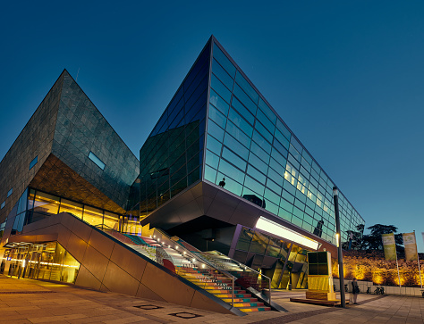 Darmstadium science center at night, west entrance on the main square in the foreground and the main facade in the background.