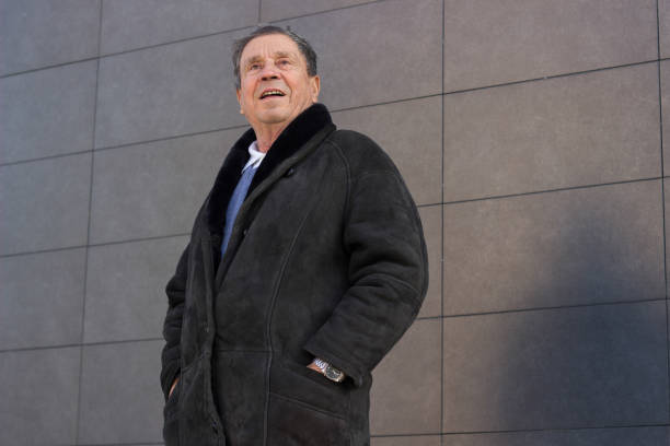 A senior ethnic businessman in his seventies is posing with his arms crossed. He wears an elegant green turtle neck sweater and eyeglasses.
