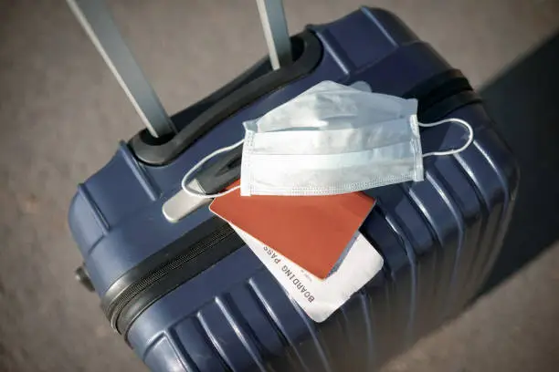 Photo of suitcase, passport and medical mask