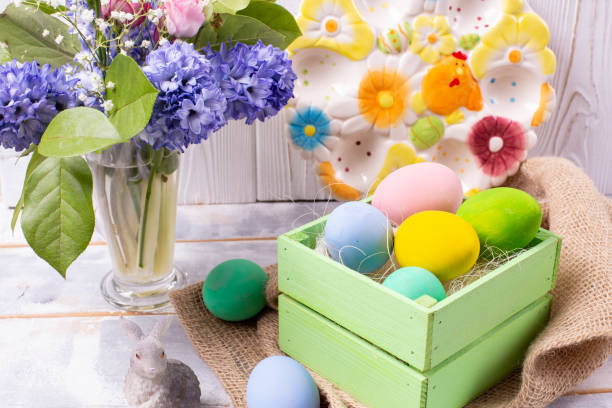 istock Easter composition with colorful eggs in a wooden crate, a rabbit figurine and a spring bouquet in a vase and an Easter ceramic plate on a white wooden table 1214363401