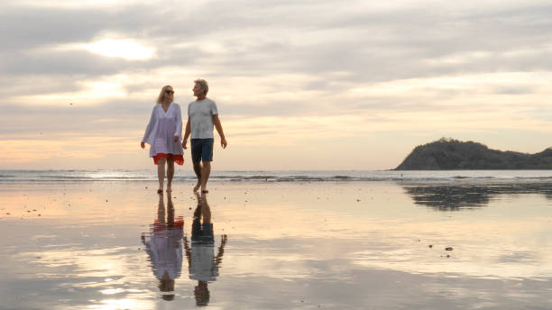 istock Couple walk along beach at sunrise 1214367019