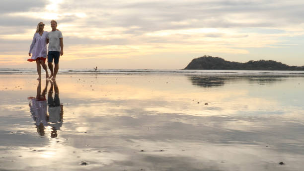 istock Couple walk along beach at sunrise 1214367046