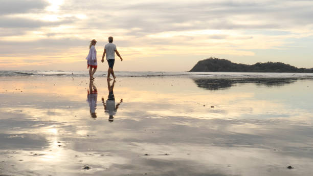 istock Couple walk along beach at sunrise 1214367082