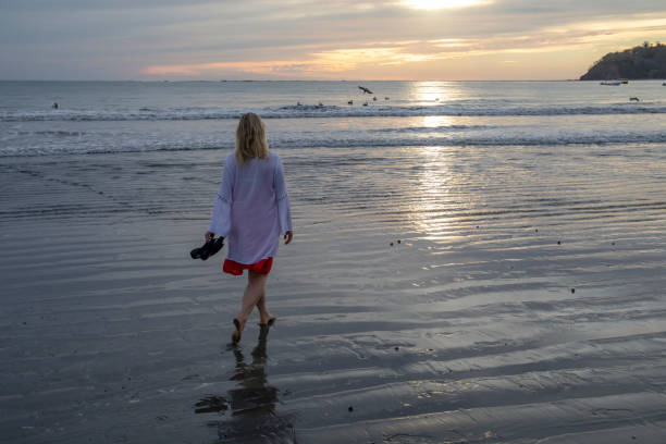istock Woman walks along beach at sunrise 1214367125