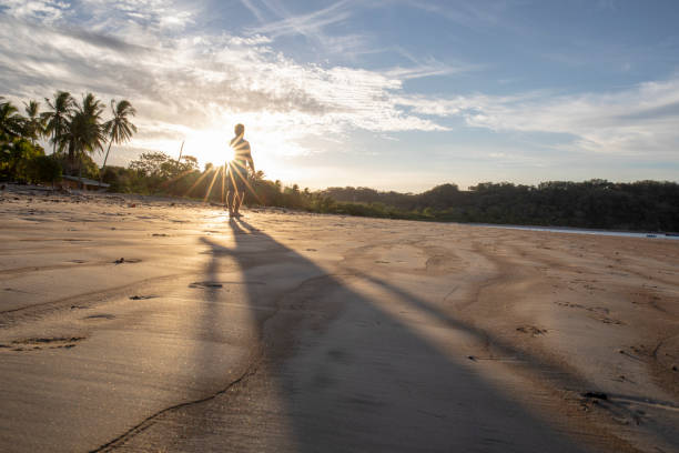 istock Man walks along beach at sunrise 1214367664