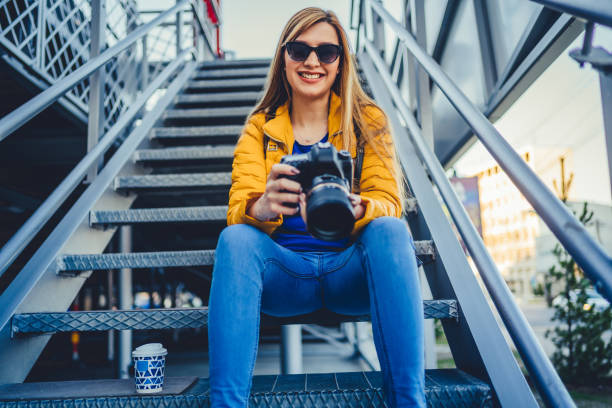 Young smiling woman with her camera sitting on stairs, checking photos outdoor