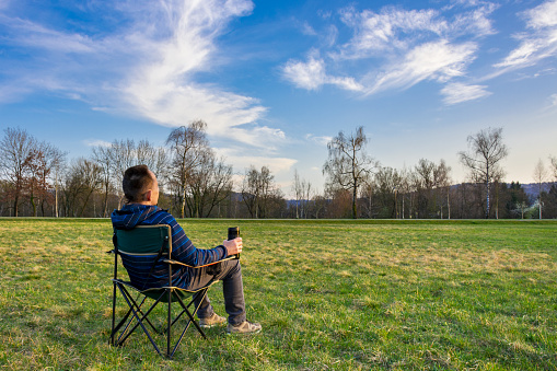 Solitary man sitting on a meadow looking into the blue sky at sunset - living with coronavirus