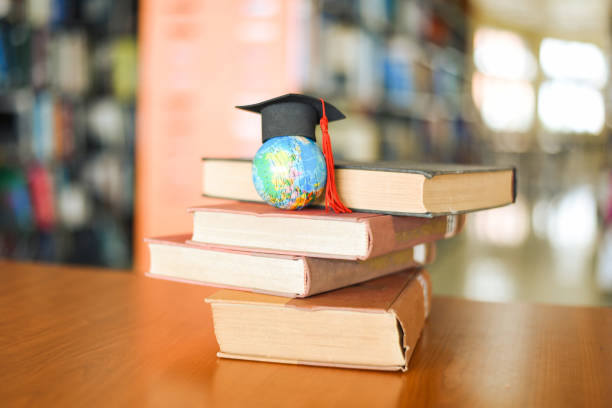 istock Books on the table in the library - Education learning old book stack and graduation cap on earth globe model on wood desk and blurred bookshelf room background 1214372493