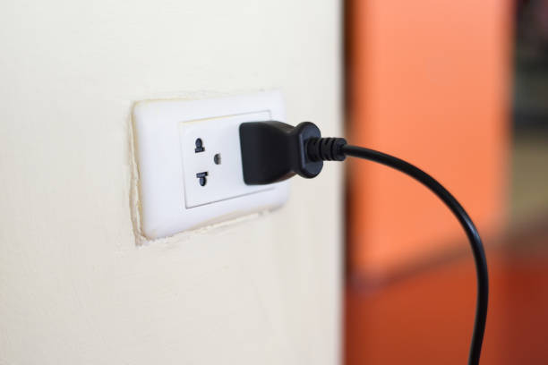 istock Home outlet plug is plugging socket on wall with black power cord cable - Power plug connecting electrical plug 1214372505