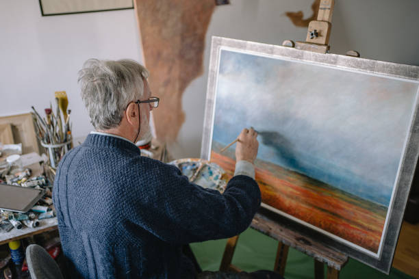istock Senior man finishing a painting in a art studio 1214373414