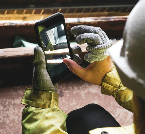 Architect holding a smartphone on construction site. young construction worker is using mobile phone on site. Construction worker with building plans and cellphone. Focus on mobile. warm vivid filter. Top view of two construction workers wearing hardhats arquitecto sosteniendo un teléfono inteligente en la obra. joven trabajador de la construcción está utilizando el teléfono móvil en el lugar. trabajador de la construcción con planos de construcción y teléfono celular. concéntrese en el móvil. fi